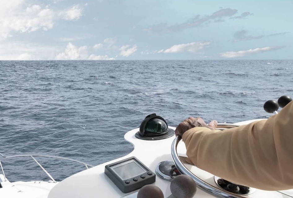 A captain's hand on the helm beside the compass, heading out across open ocean